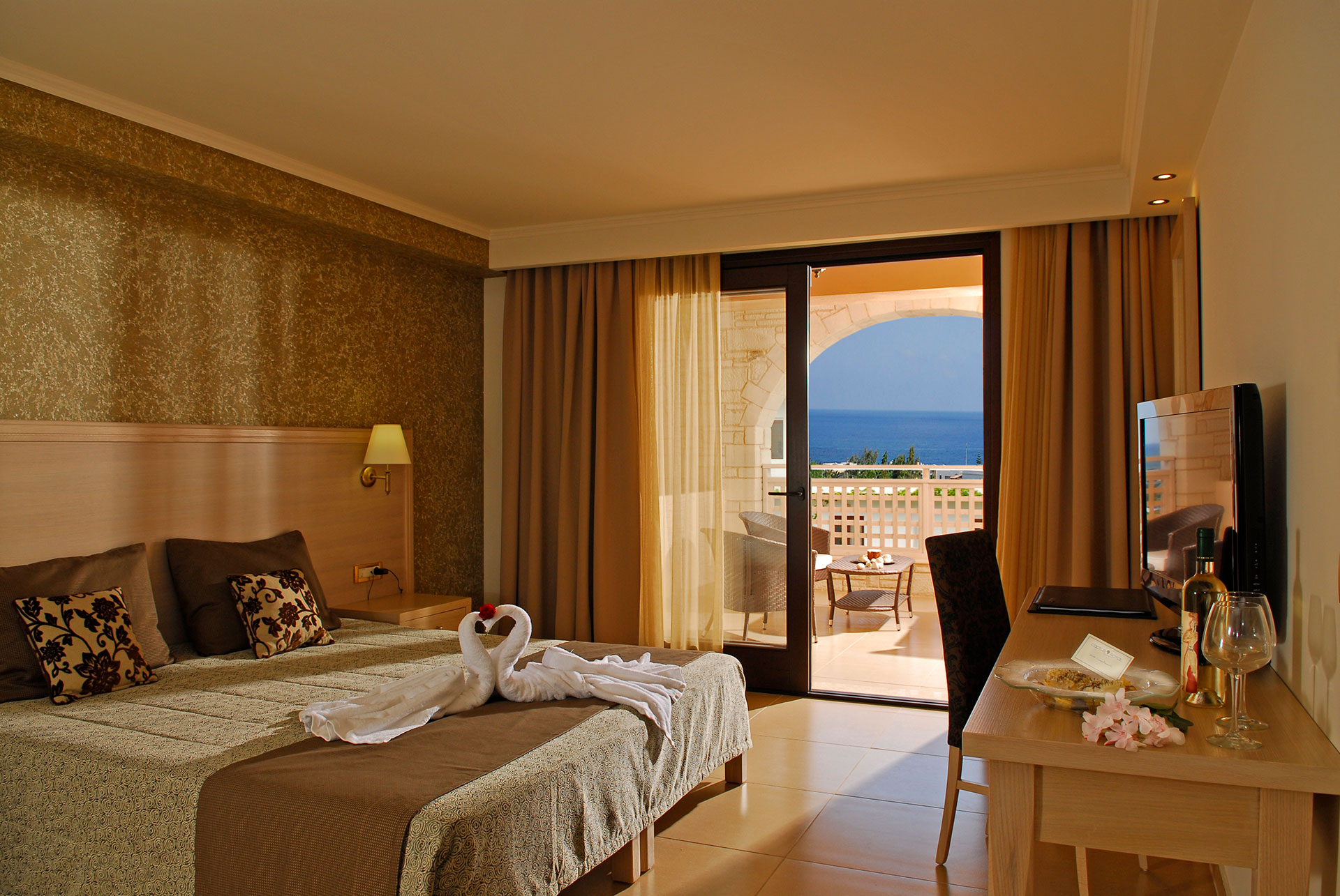 Δωμάτιο ξενοδοχείου με διπλό κρεβάτι χρώματος άσπρου και πρασίνου μαζί με τραπέζι και μπαλκόνι το απόγευμα