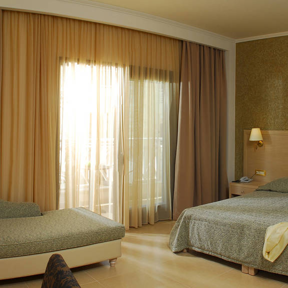 White and green hotel room with a double bed and a single view of the room with closed curtains