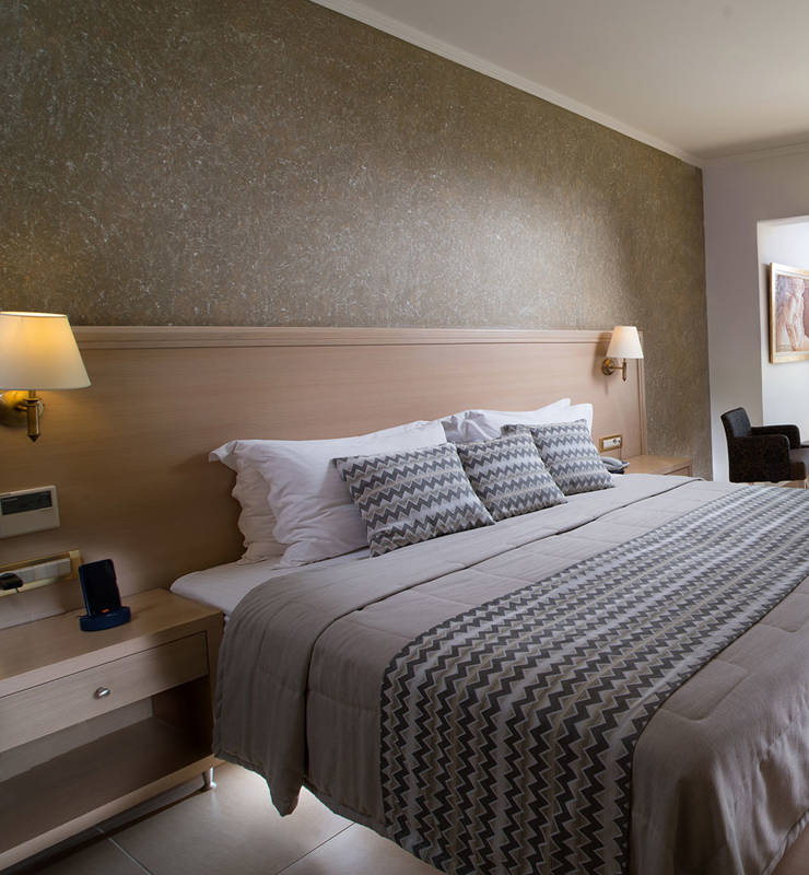 Interior view of a hotel room with a white double bed with gray wallpaper and a brown coffee table
