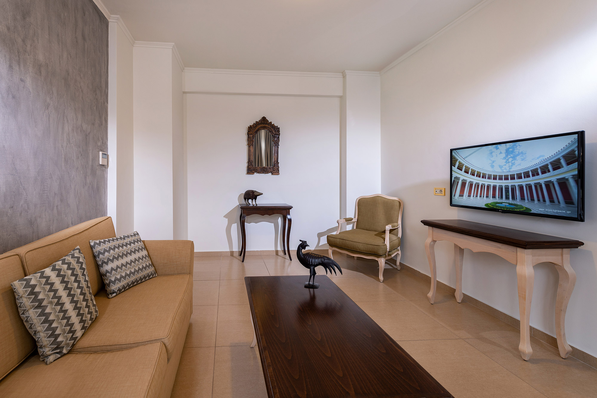 Hotel room with white color and gray wallpaper and gray curtains with a beige sofa with a green armchair two tables and a television and a mirror