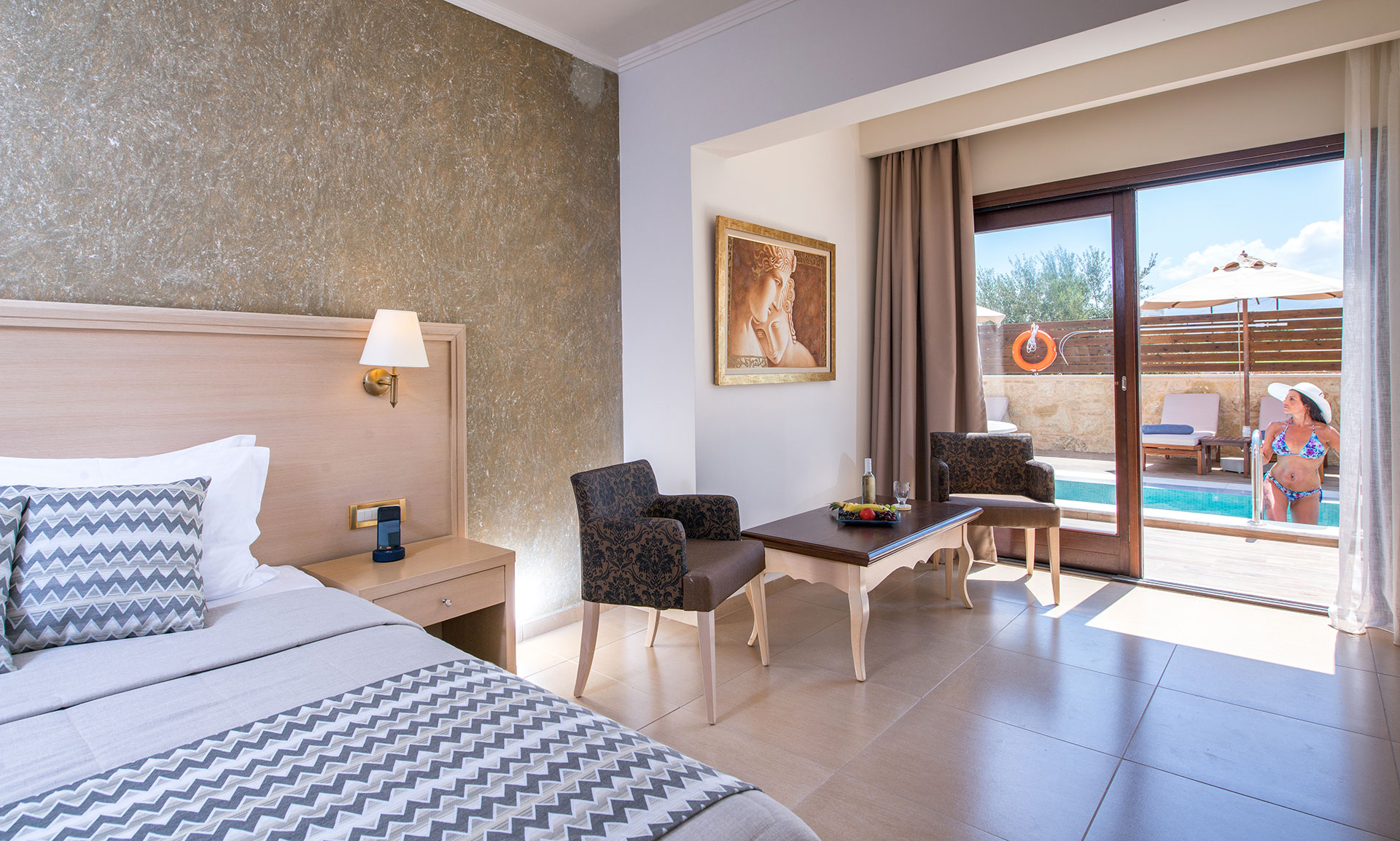 Right view of a hotel room with a white double bed with beige wallpaper and a coffee table and exit to the pool