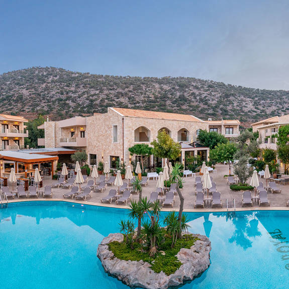 Resort with mountain view and large swimming pools with sunbeds and umbrellas, at Stalis Crete