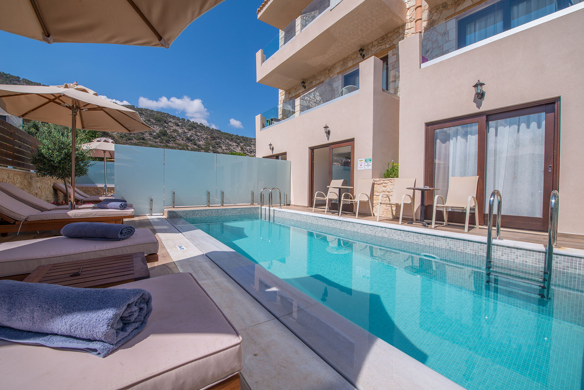 Δύο δωμάτια ξενοδοχείου τα οποία περιέχουν πισίνα με θέα το βουνό, τον ουρανό και δύο σέτ ξαπλώστρες